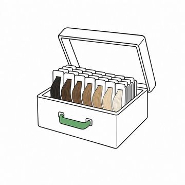 Line illustration: a wooden card-index box with its lid tipped back, filed inside where the record cards should be a tight row of hair-colour swatch strands on blank unmarked tabs, one swatch strand and the box's pull handle the accent colour